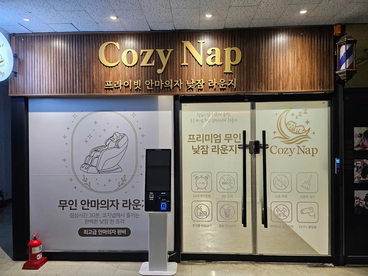 무인 안마의자 라운지 코지냅 매장 입구: 'Cozy Nap 프라이빗 안마의자 낮잠 라운지' 간판, 유리문, 왼쪽에 결제 키오스크가 서 있다